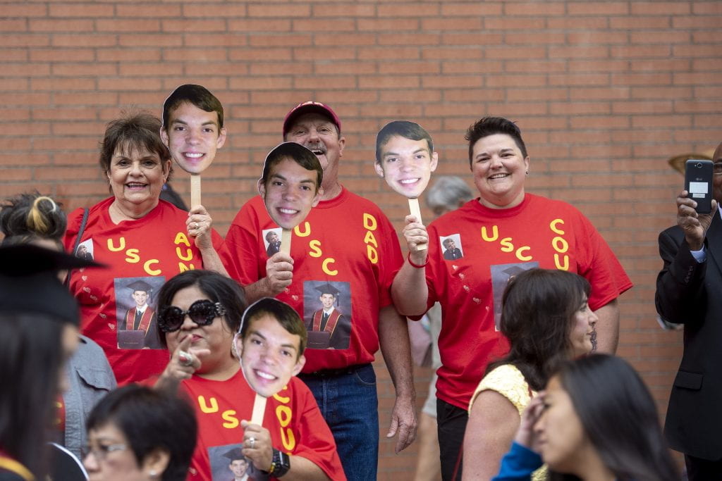 Trojan families decked out in USC tees holding up signs with their students' faces